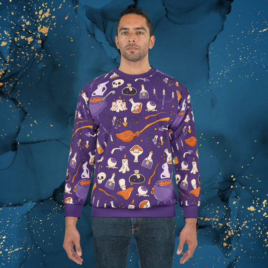Man wearing a purple unisex crewneck sweatshirt with all-over witchy potions and Halloween-themed pattern including skulls, candles, cauldrons, and bottles. Displayed against a dark blue artistic background with gold splatter accents. Invaluable Minutia spooky season exclusive.