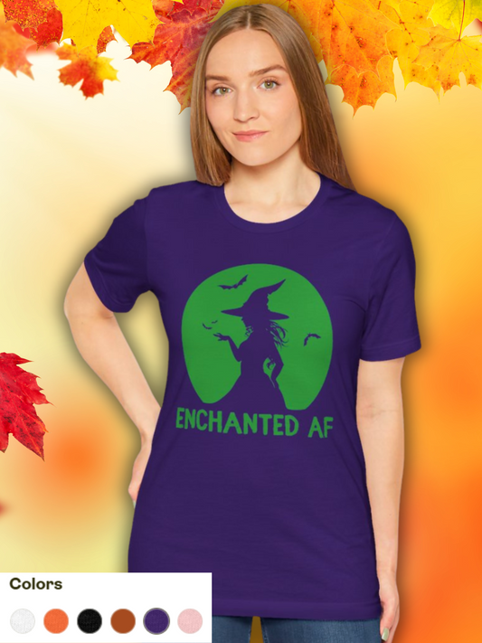 Woman wearing a purple Bella+Canvas unisex t-shirt with green witch silhouette and ‘Enchanted AF’ text graphic. Styled against an autumn leaf background for Halloween season. Invaluable Minutia exclusive.