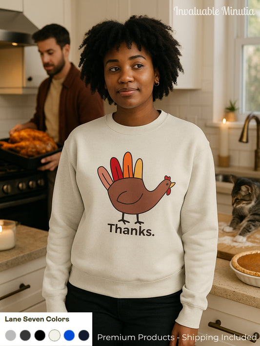 Woman wearing a cream Lane Seven sweatshirt with a minimalist Thanksgiving turkey design that says “Thanks.” standing in a cozy kitchen while someone prepares a holiday meal in the background.