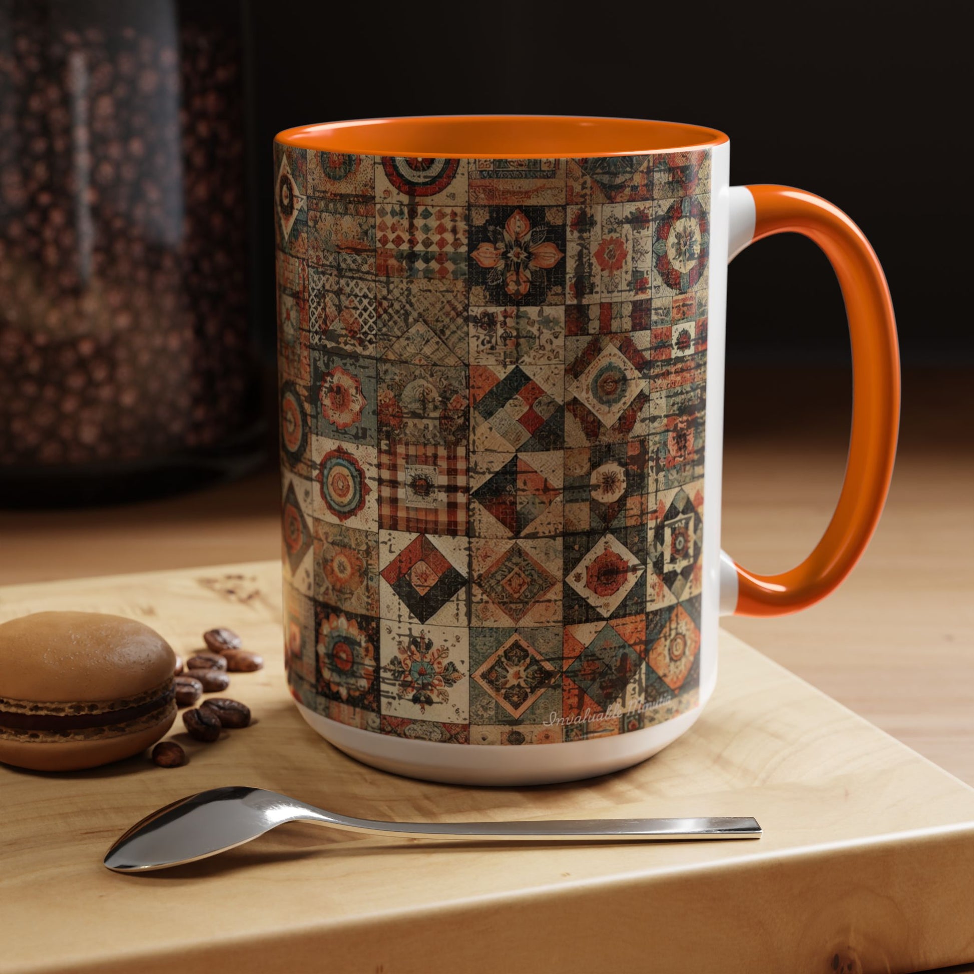 Right-side lifestyle view of 15oz Boho Patchwork Quilt ceramic coffee mug with orange accent handle and interior — premium white ceramic mug featuring intricate patchwork quilt pattern in rustic boho tones. Displayed on a wooden surface with coffee beans, macaron, and spoon. Boutique mug by Invaluable Minutia. InvaluableMinutia.com